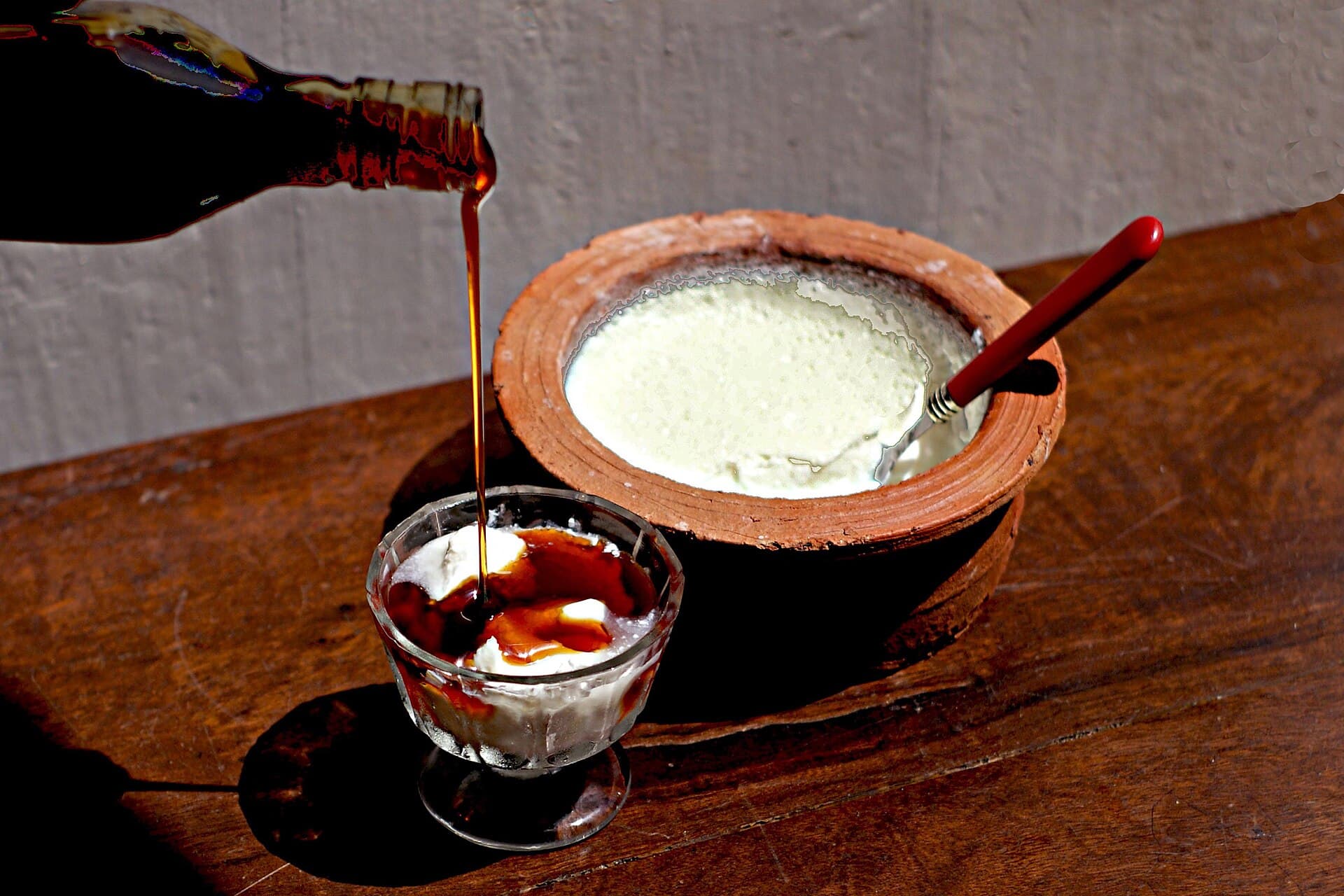 Kithul treacle poured over buffalo curd in a glass bowl, beside the clay pot it was set in