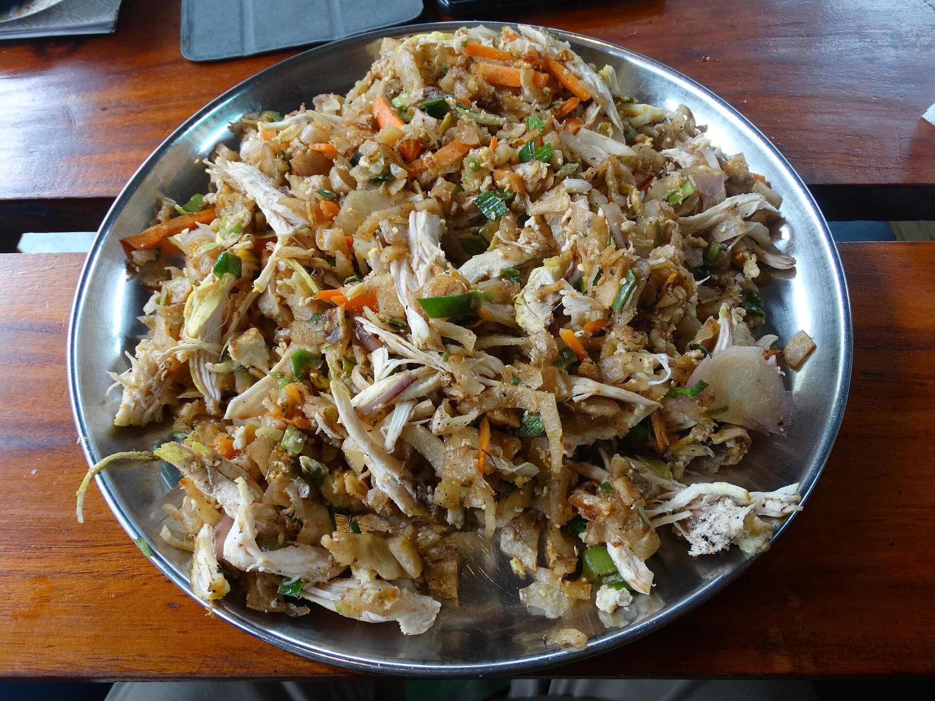 A steel platter of chicken kottu roti on a wooden table in Ella