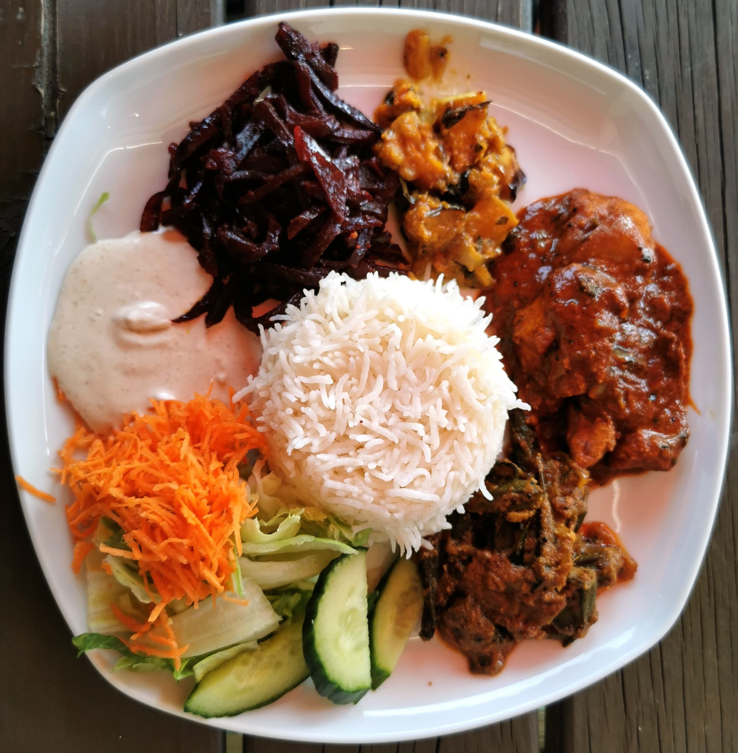 A Sri Lankan rice and curry plate: rice ringed by chicken curry, beetroot, potato, okra, raita, grated carrot and cucumber