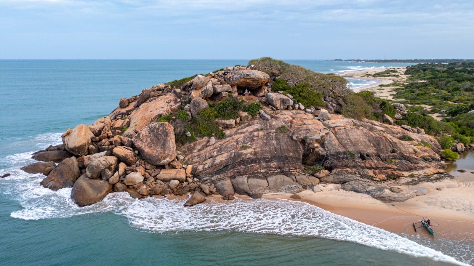 A granite headland rising from the sand where the surf meets it